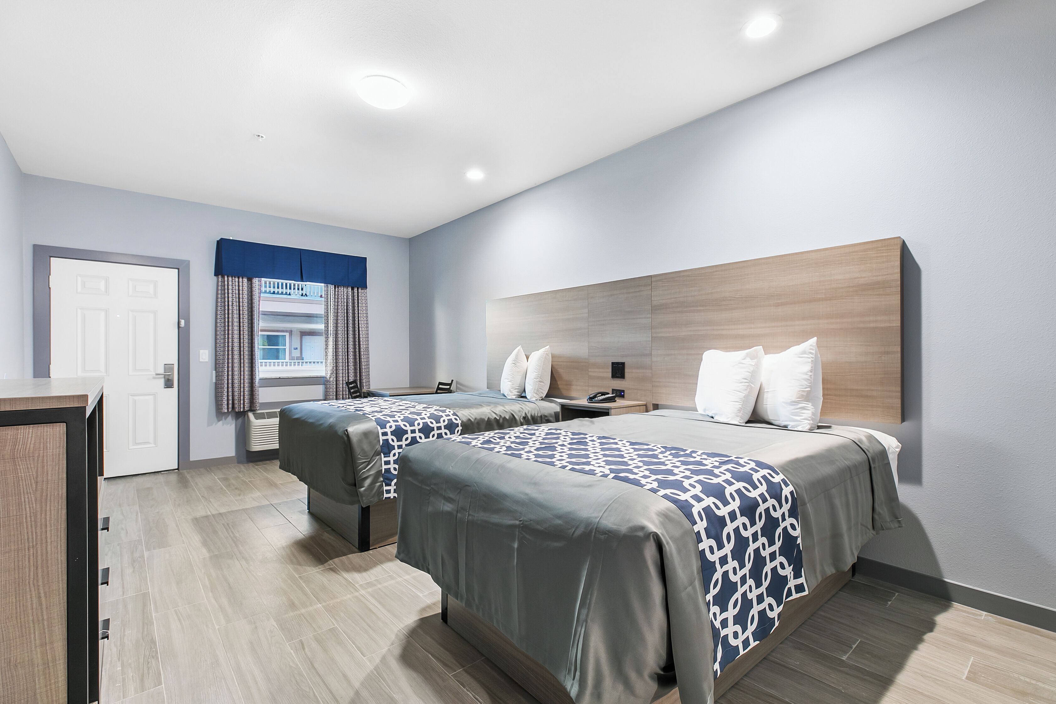 Et moderne hotelværelse med to senge, et skrivebord og et stort vindue med gardiner.