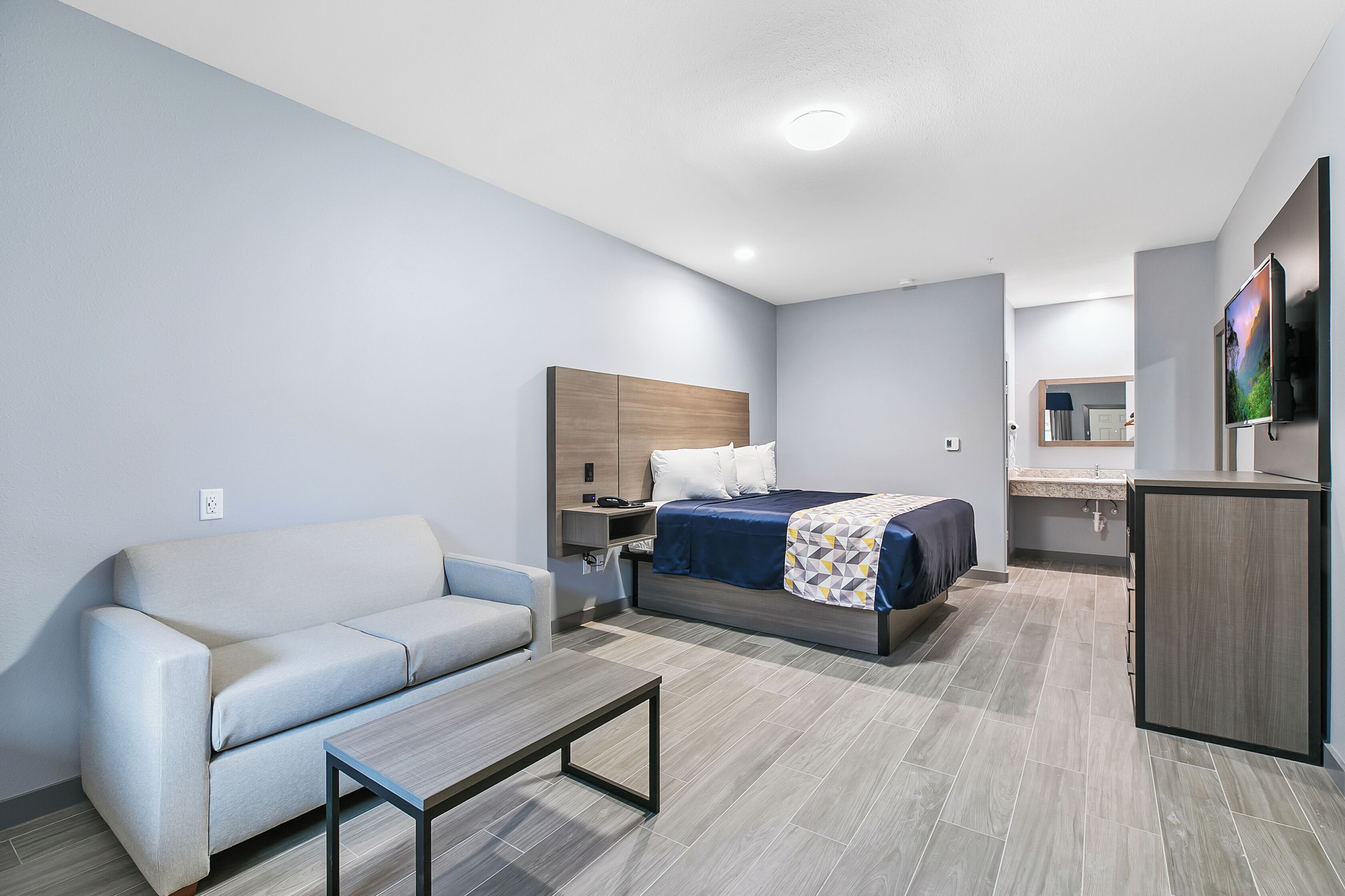 A modern hotel room with a bed, a sofa, a desk, and a TV.