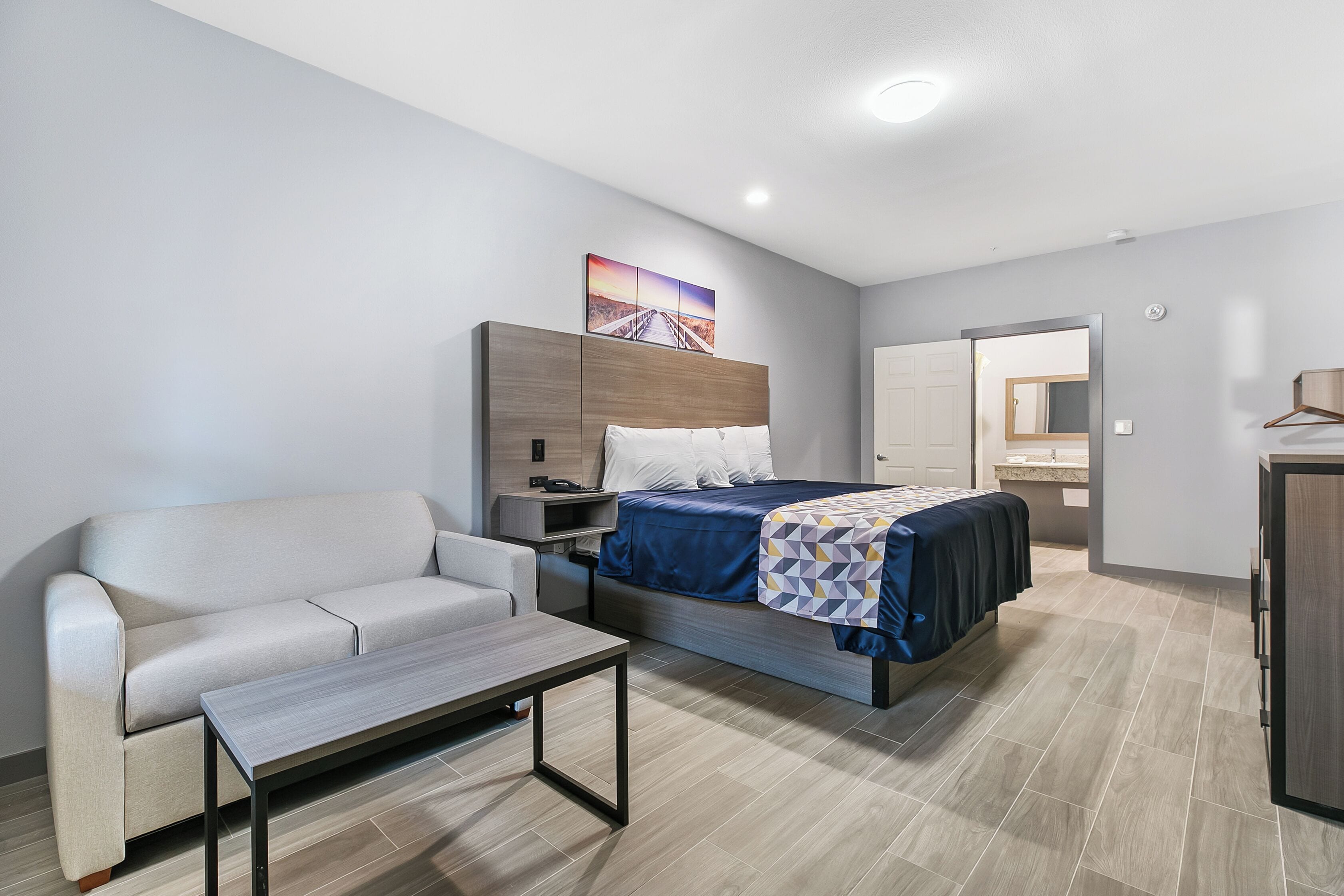 A modern hotel room with a bed, a sofa, a bedside table, and a nightstand.