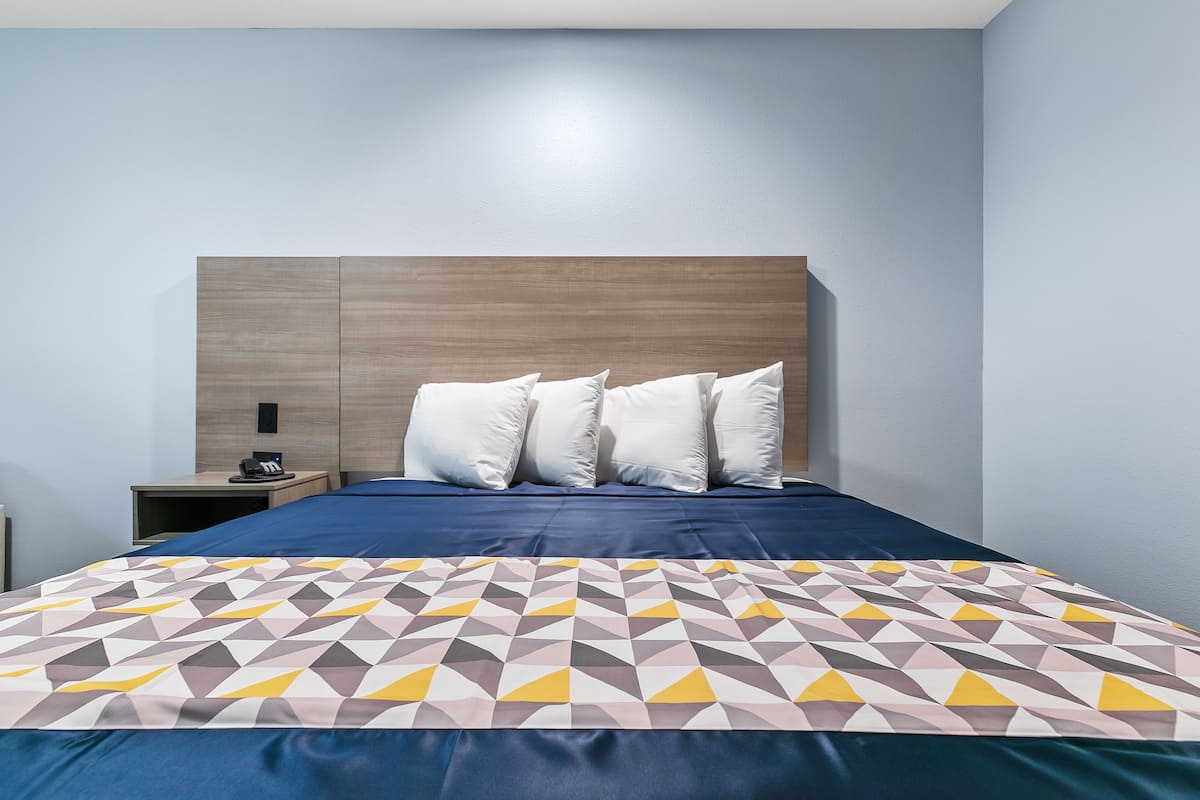 Una cama bien hecha con un edredón estampado con motivos geométricos, un cabecero de madera y almohadas blancas.