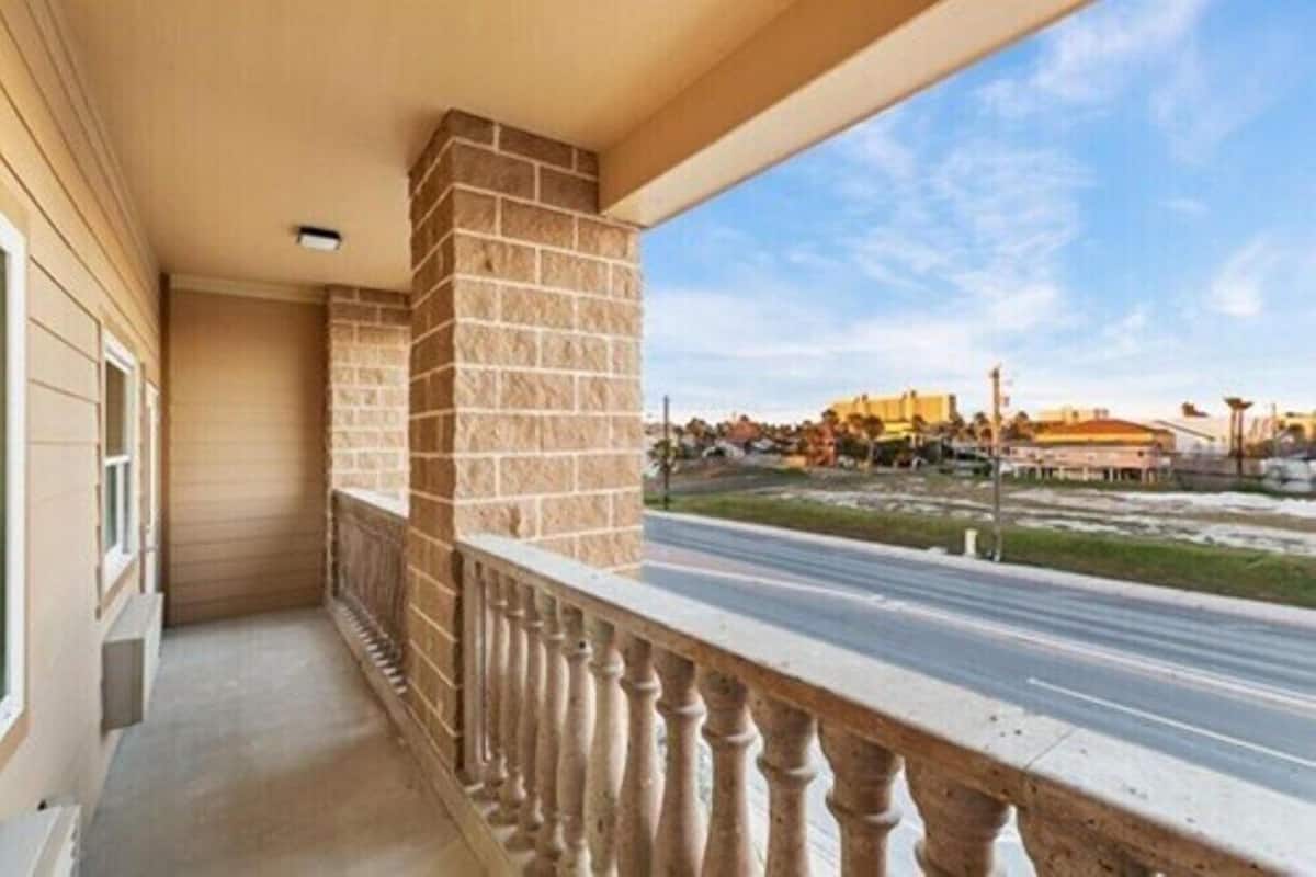Un balcón con un pilar de piedra, vista a una carretera y edificios a lo lejos.