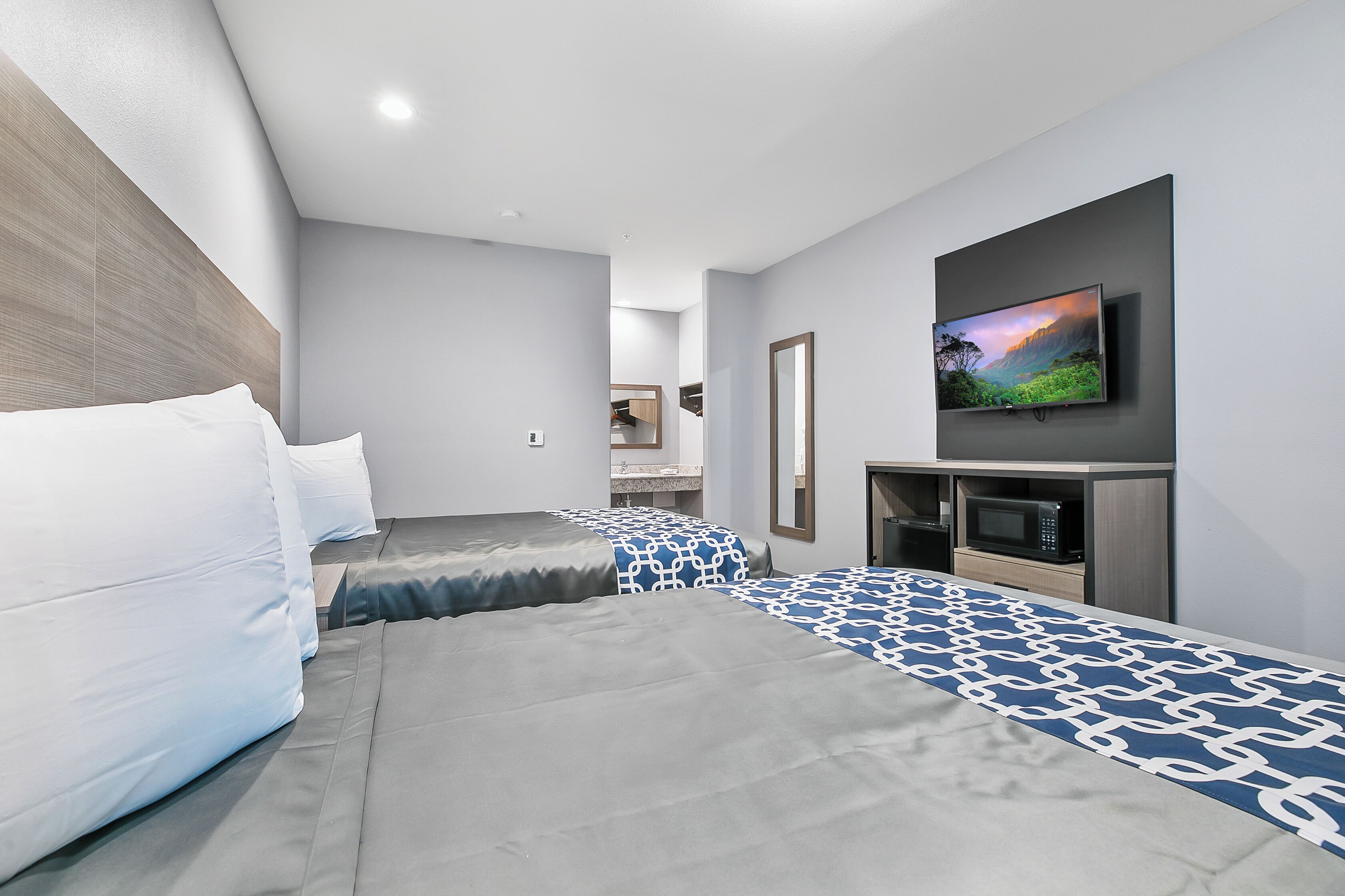A modern hotel room with a large bed, a flat-screen TV mounted on the wall, and a microwave in the corner.