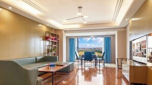 Habitación de hotel con sofá, mesa de centro, zona de comedor con sillas y vistas a través de un ventanal.