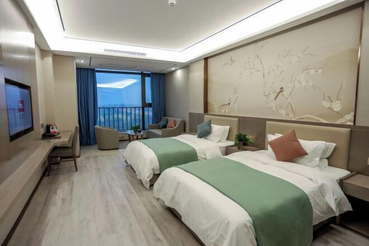 A hotel room with two beds, a desk, a chair, a TV, and a balcony with a view.