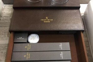 Una caja de cuero marrón con el nombre de la marca 'Samantha' y un par de gafas encima. En su interior, hay varias cajas negras con letras doradas, una de ellas etiquetada como 'SHOWER CAP'.