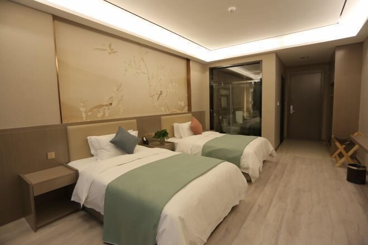 A hotel room with two beds, a small bedside table, a large wall mural, and a glass shower enclosure.