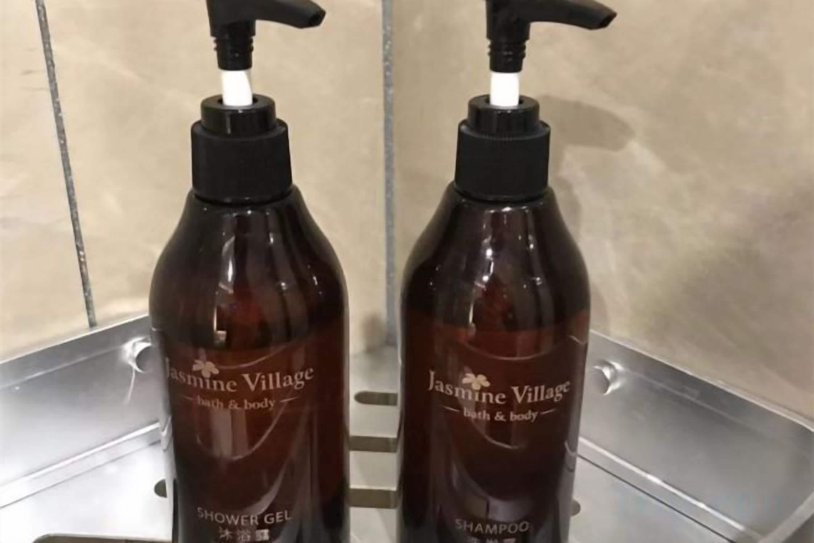 Deux bouteilles de gel douche et de shampoing de la marque Jasmine Village, posées sur une étagère en métal.