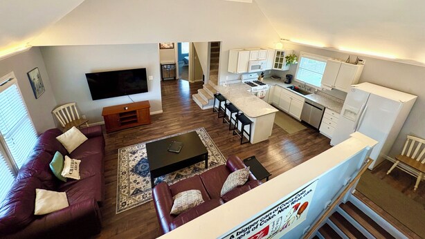 A spacious living area with a TV, sofa, and coffee table, a kitchen with white cabinets, and a staircase leading to an upper level. - Mass Ave & Bottleworks + Garage parking (Indianapolis)