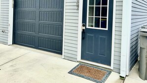 A garage door and a front door with a window, both in a light gray siding house. - Mass Ave & Bottleworks + Garage parking (Indianapolis)