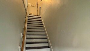A staircase with white walls and dark steps leading upwards. - Mass Ave & Bottleworks + Garage parking (Indianapolis)