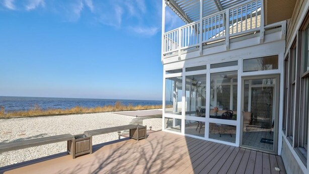 Ein Strandgrundstück mit einer Holzterrasse, Glastüren und einem Balkon mit Blick auf den Ozean.