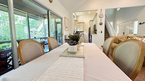 A spacious dining area with a long table, chairs, and a view of greenery through large windows. - Free Daily Golf Villa · Private Island · 4BR/4BA · 25 min to Hilton Head (Okatie)