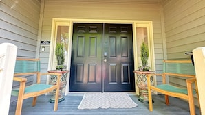 A front porch with a dark wooden double door, two wooden chairs with green cushions, and two potted plants. - Free Daily Golf Villa · Private Island · 4BR/4BA · 25 min to Hilton Head (Okatie)