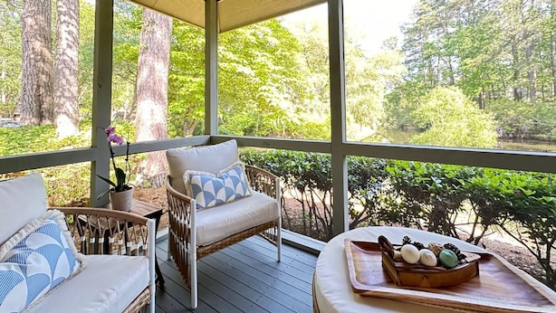 A covered porch with wicker furniture, a wooden table with a tray of eggs, and a view of a forested area. - Free Daily Golf Villa · Private Island · 4BR/4BA · 25 min to Hilton Head (Okatie)