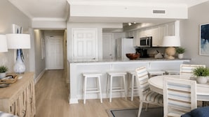 A modern kitchen with white cabinetry, a central island with stools, and a dining area with striped chairs.