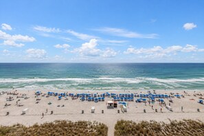 Una playa con hileras de sombrillas azules y tumbonas, una orilla arenosa y el océano al fondo.