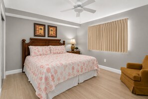 A bedroom with a bed, a nightstand, a lamp, a ceiling fan, a window with curtains, and a chair. - Book Now! Fall on the Beach! Starbucks! Emerald Beach Resort. Beach Service! (Panama City Beach)