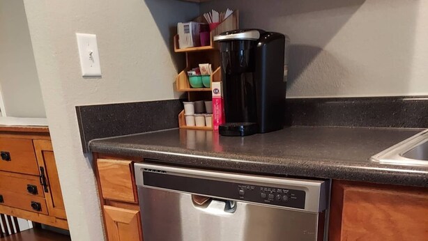 A stainless steel dishwasher in a kitchen with wooden cabinets and a black countertop. - Chateau Rose (Branson)