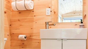 A wooden cabin bathroom with a toilet, sink, and towel rack. - Trailside Stays - Tiny House in the Woods-Escape to Nature. Robin (Dorchester)