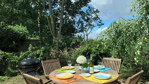 Une terrasse en bois avec une table ronde dressée pour un repas, entourée de chaises.