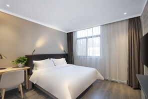 Una habitació d'hotel amb llit, escriptori, cadira i una finestra gran amb cortines.