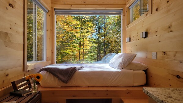 Ein gemütliches Schlafzimmer mit einem großen Fenster und Blick auf Herbstbäume.