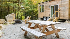 Una cabaña de madera con una mesa y sillas de picnic, rodeada de un bosque.