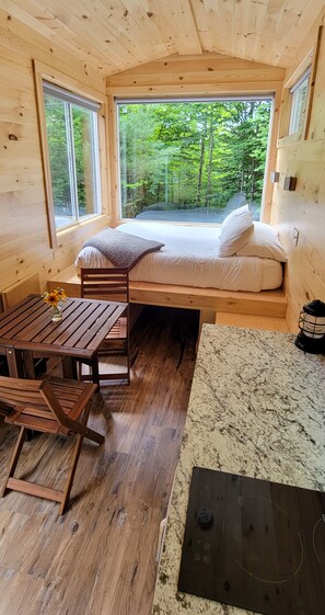 Ein gemütliches Blockhaus mit einem Bett, Holzmöbeln und großen Fenstern mit Blick auf einen Wald.