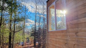 Una cabaña de madera con un ventanal grande, rodeada de un área boscosa.
