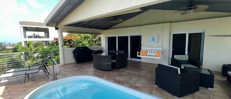 A covered outdoor area with a swimming pool, patio furniture, and a view of the surrounding landscape.