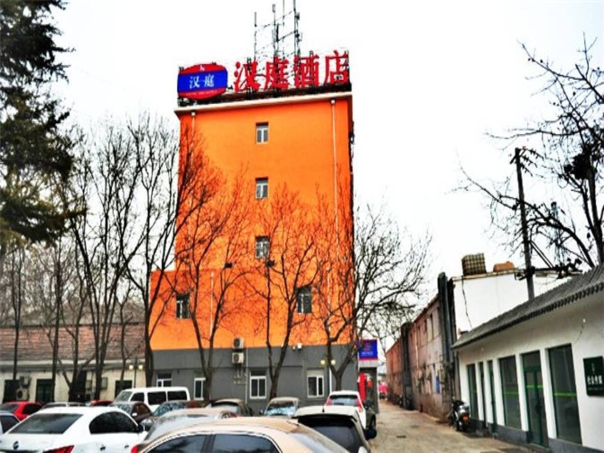A tall building with a red sign, parked cars, and leafless trees.