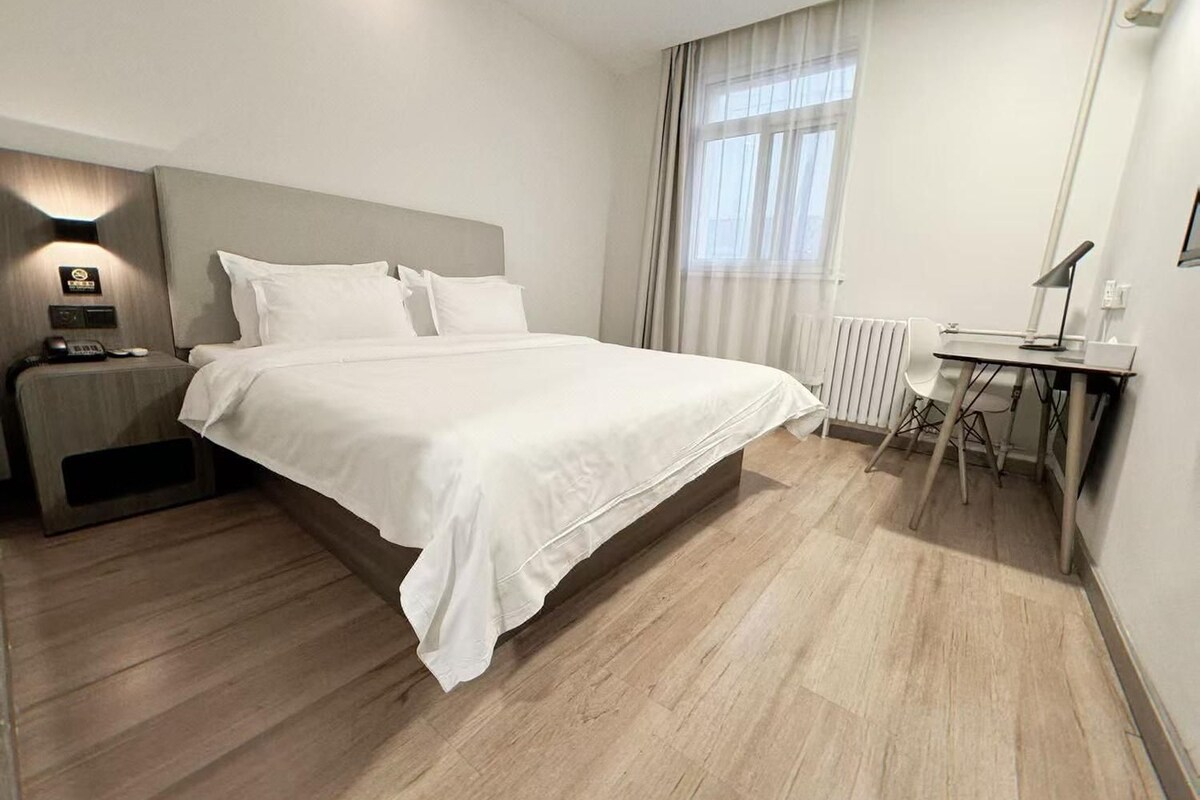 Ein modernes Hotelzimmer mit einem großen Bett, einem Schreibtisch und einem Fenster mit Vorhängen.
