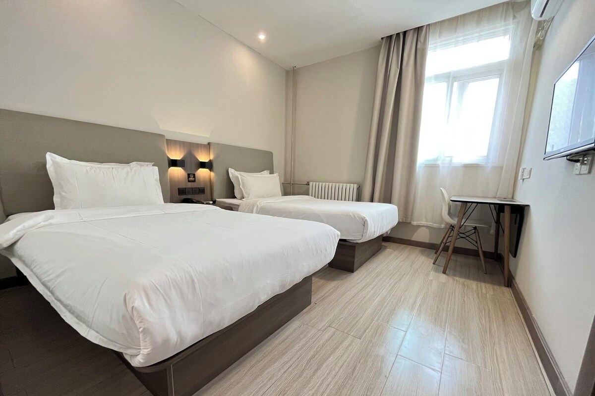 Ein Hotelzimmer mit zwei Betten, einem Schreibtisch, einem Sessel, einem Heizkörper und einem Fernseher.