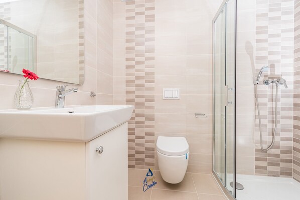 A bathroom with a glass shower enclosure, a white sink with a vase of flowers, and a toilet.