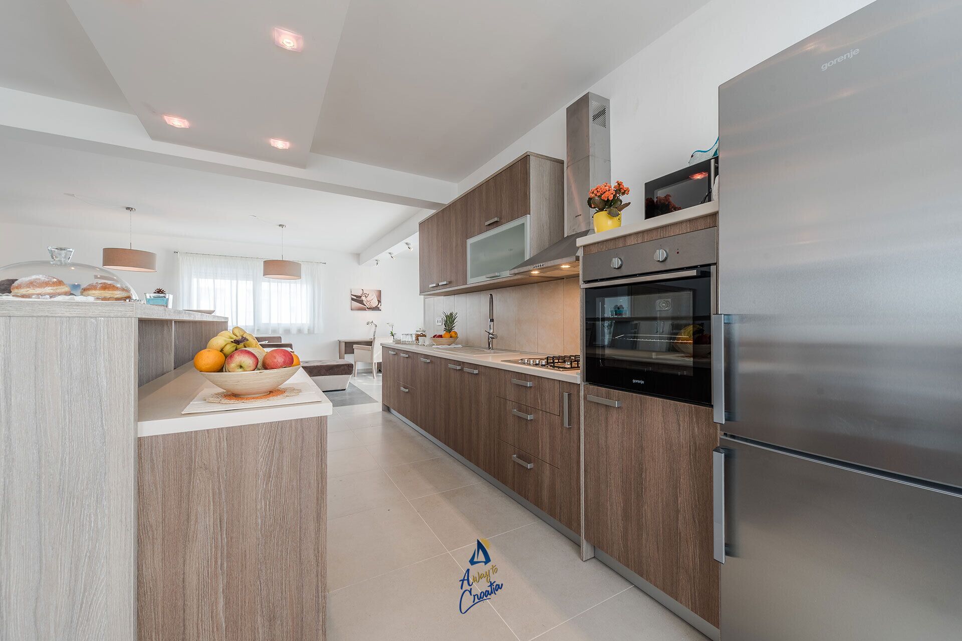 A modern kitchen with wooden cabinets, stainless steel appliances, and a central island with fruit.