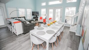 Un salón amplio con techo alto, una mesa de comedor con sillas, un sofá y un televisor.