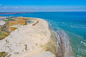 Vue aérienne d’une zone côtière avec une plage de sable, un petit village composé de quelques bâtiments et un océan bleu et limpide.