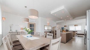 A modern kitchen with a central island, a dining area with a table and chairs, and a living area with a sofa and a TV. - Modern 4 BD villa with heated pool for up to 8 guests (Sukošan)