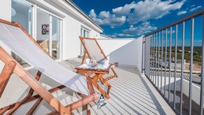 A balcony with two wooden lounge chairs, a glass door leading to a room, and a view of a coastal landscape. - Modern 4 BD Villa with Heated Pool near Beaches (Sukošan)