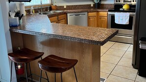 Una cocina con armarios de madera, microondas, horno, lavamanos y una zona de bar con taburetes.