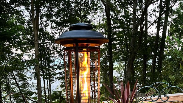 Una terraza de madera con un farol de metal, dos sillas de mimbre y una planta en maceta.
