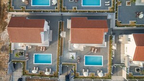 An aerial view of a resort with multiple pools, each surrounded by lounge chairs and umbrellas, and buildings with red-tiled roofs. - Exquisite 4 BD villa for 8 with heated pool near Zadar (Sukošan)