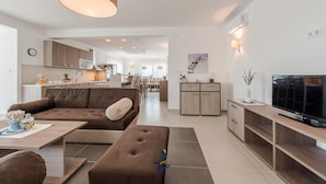 Un soggiorno moderno con un divano, poggiapiedi e una TV su un mobile in legno.