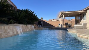 A swimming pool with a waterfall feature, surrounded by a stone wall and palm trees. - Perfect Las Vegas Private Retreat w/ Pool & Spa! (Las Vegas)