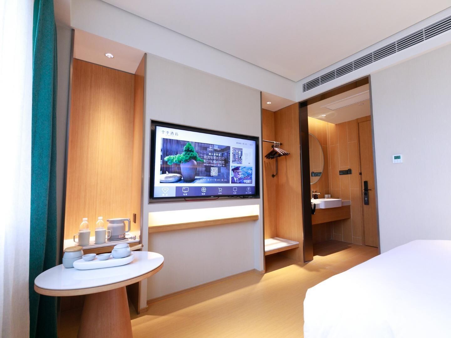 A modern hotel room with a bed, a TV mounted on the wall, a small table with cups and a tray, and a wooden wardrobe.