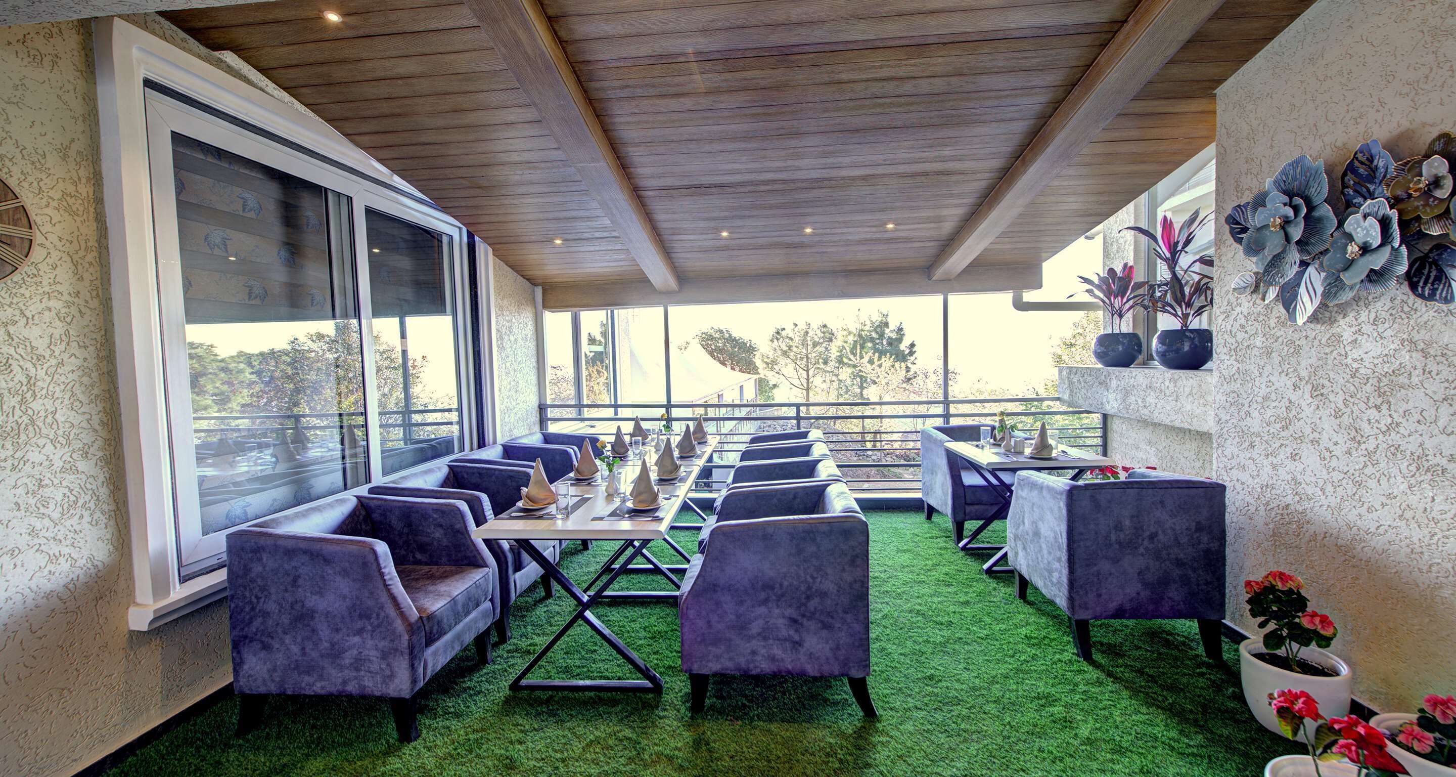 Un área de estar al aire libre techada con piso de césped artificial verde, sillas acolchadas y mesas dispuestas para comer.