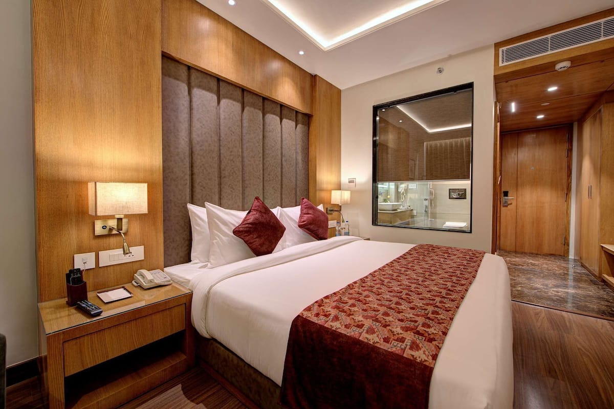 A hotel room with a large bed, wooden headboard, bedside lamps, a nightstand, and a mirror.