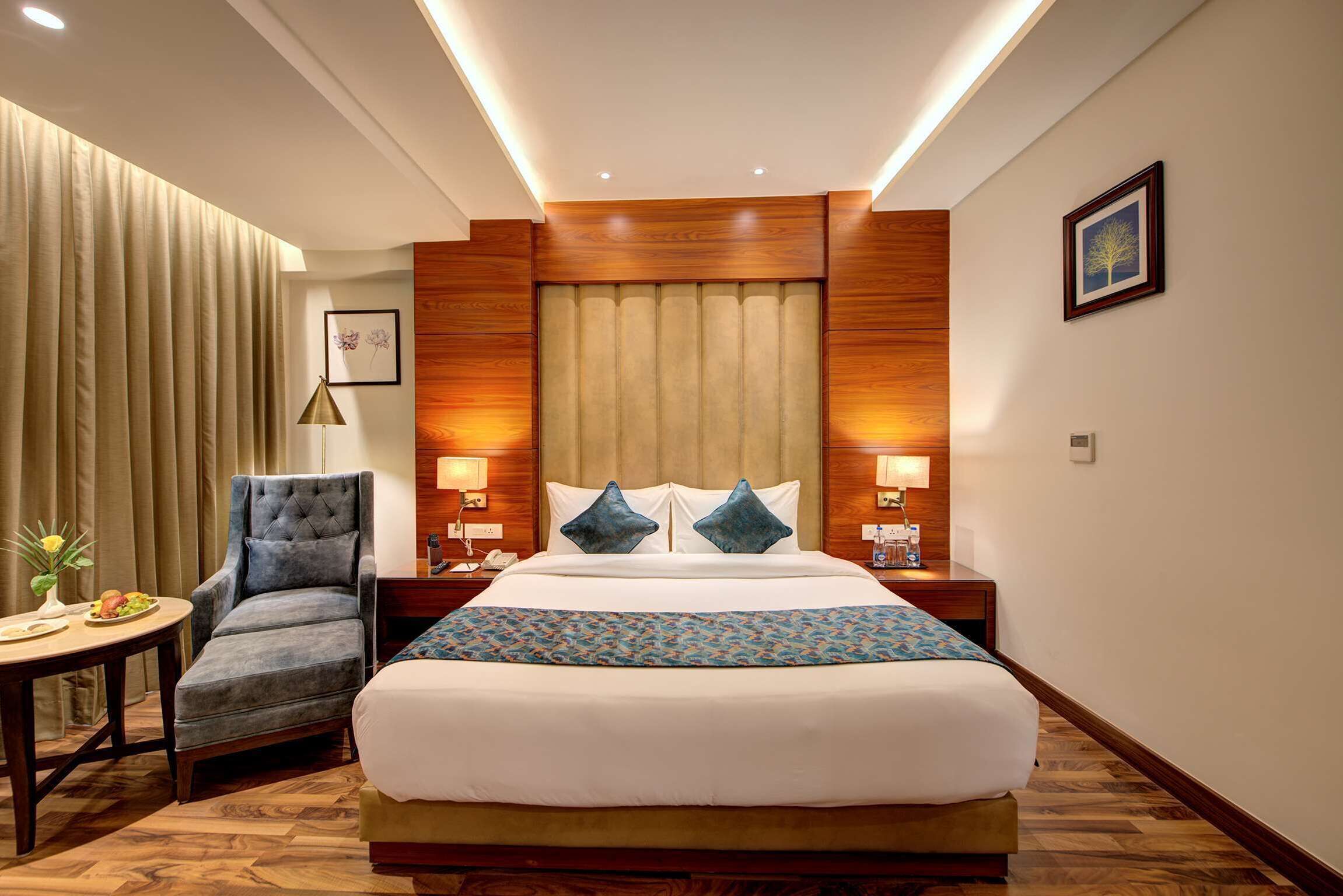 A hotel room with a large bed, a chair, a table with a vase of flowers, and wooden paneling on the walls.