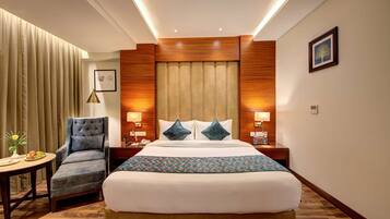 A hotel room with a large bed, a chair, a table with a vase of flowers, and wooden paneling on the walls.