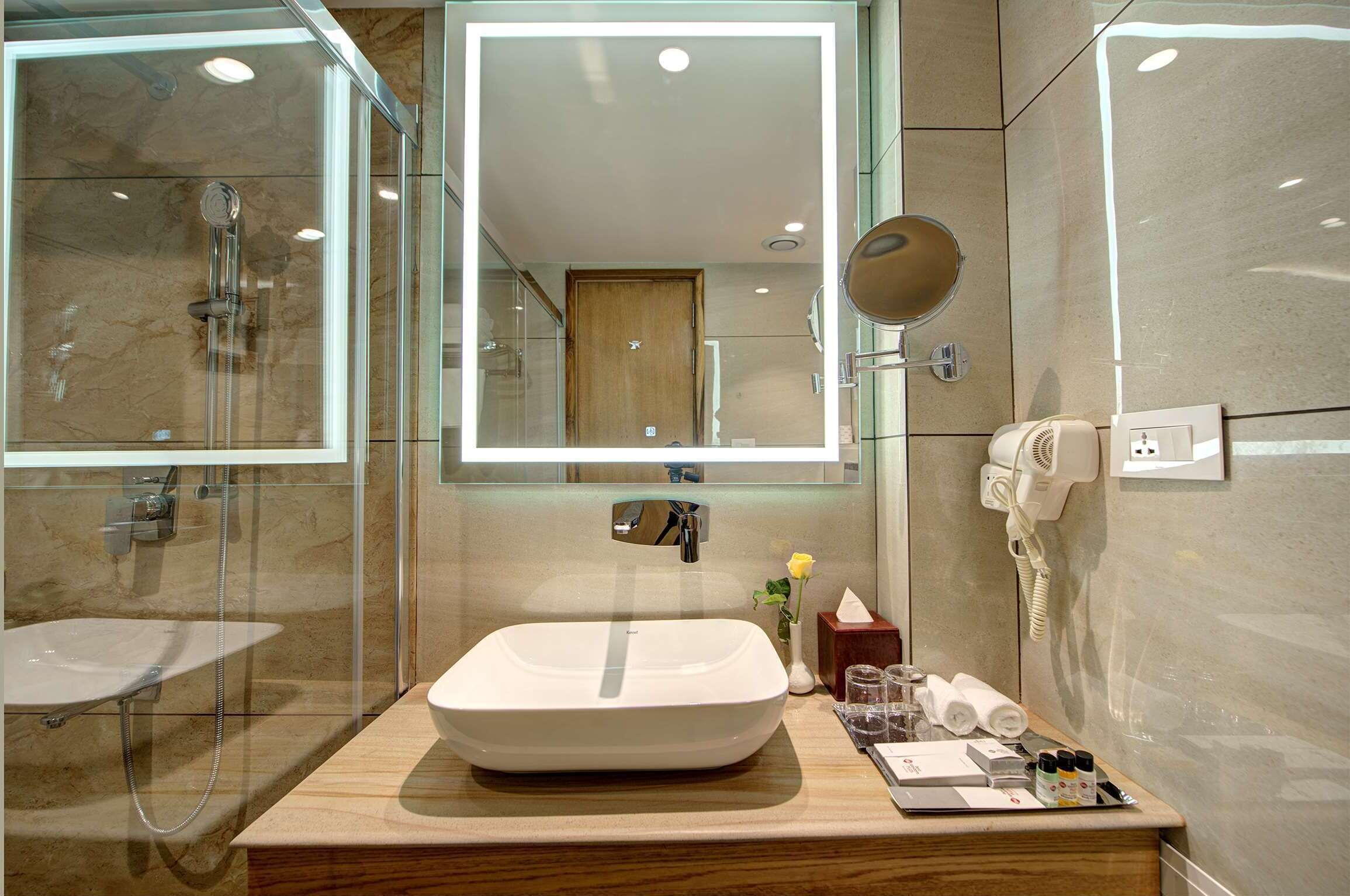 Une salle de bain moderne avec un grand miroir, un lavabo, une douche et un sèche-cheveux.